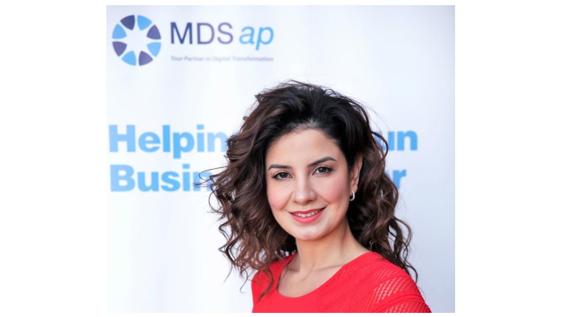a head and shoulders view of a woman executive in a red dress with the MDSap logo visible behind her