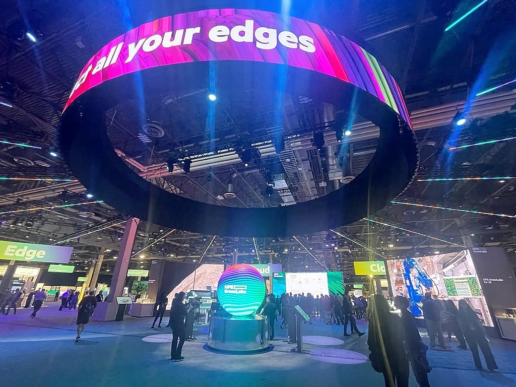 view of a colourful interior space with many hi-tech exhibition stands and an overhead display structure with lettering on it