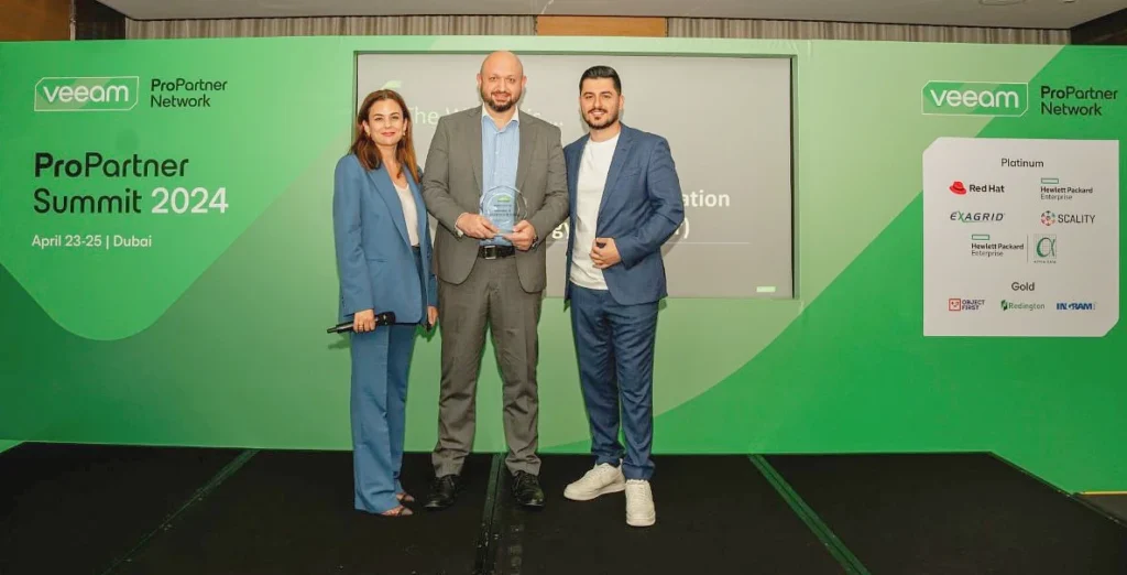three people seen on a presentation stage as one of them is holding a glass trophy