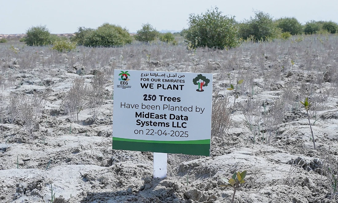 a sign is seen planted in the sandy soil of a coastal region with small saplings all around