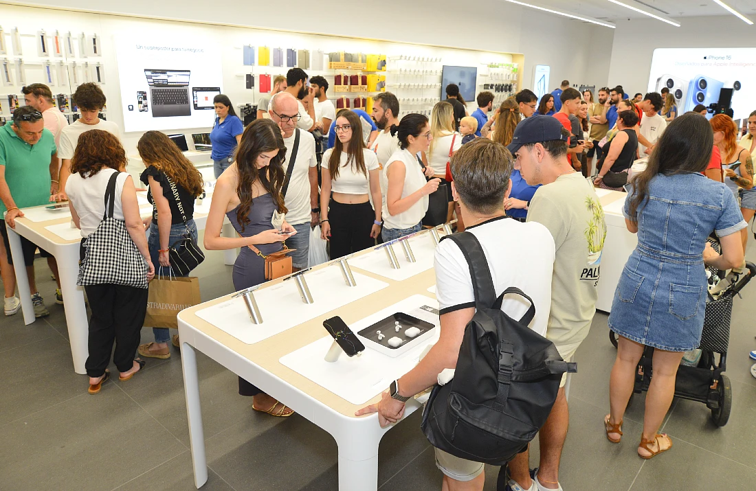 Interior of a hi tech retail site with many people present browsing the Apple devices on display