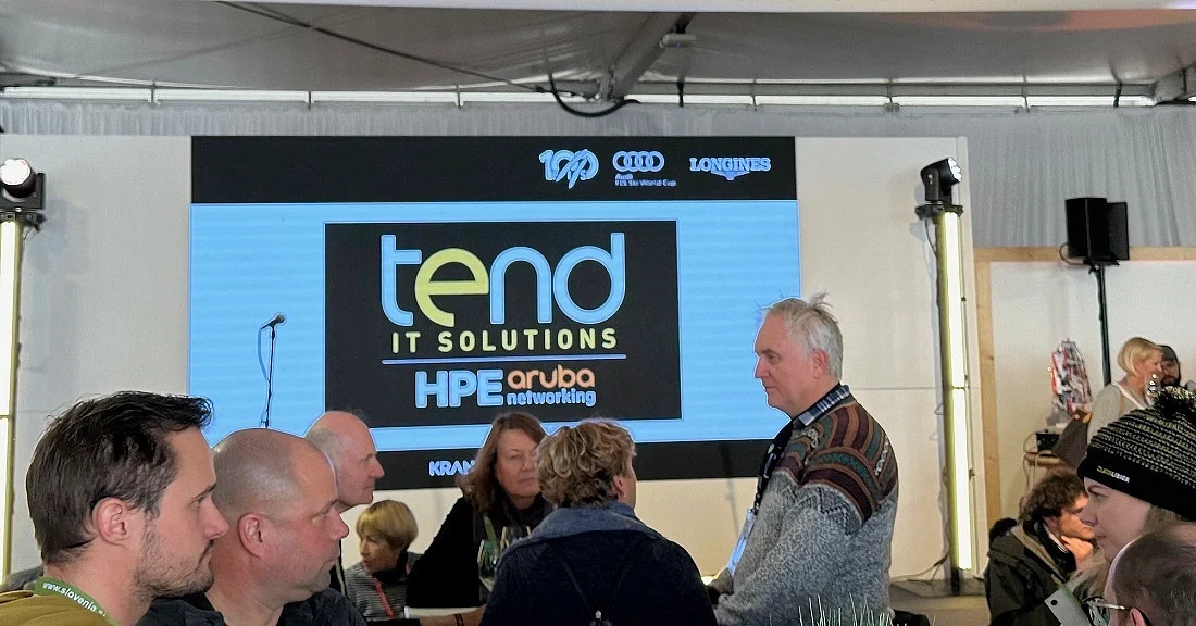 People are seen inside a media tent with a large display screen behind them.