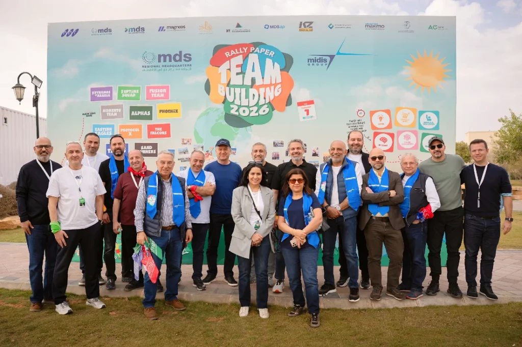 Photo de groupe des équipes Midis devant une grande banderole où l’on peut lire en évidence : « Rally Paper team building 2026 ». 