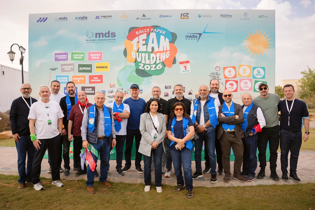Photo de groupe des équipes Midis devant une grande banderole où l’on peut lire en évidence : « Rally Paper team building 2026 ». 